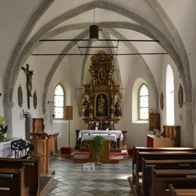 De St. Laurentiuskerk in het centrum van Feldthurns werd gebouwd tussen 1286 en 1295. In de 14e eeuw werd het herbouwd en uitgebreid. Het gevelschilderij toont de heilige Laurentius, die in de 3e eeuw als christelijke martelaar een wrede dood stierf: hij werd gegrild op een rooster. De toren werd pas in de 16e eeuw toegevoegd, maar zonder voldoende diepe funderingen. En zo is hij in de loop van de tijd opzij overgeheld en staat nu duidelijk scheef naast de St. Laurentiuskerk.